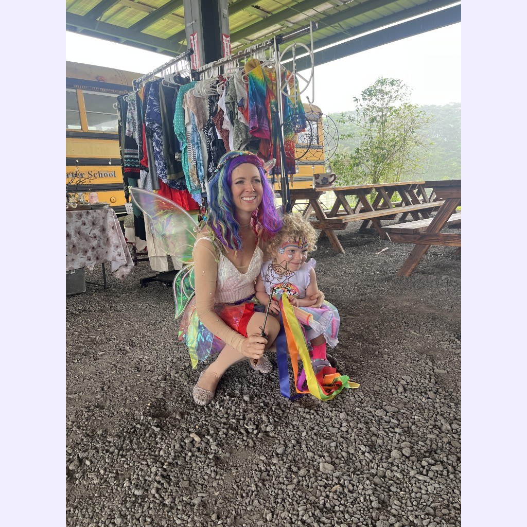 Loni in fairy costume with a young guest holding rainbow ribbons at an outdoor event