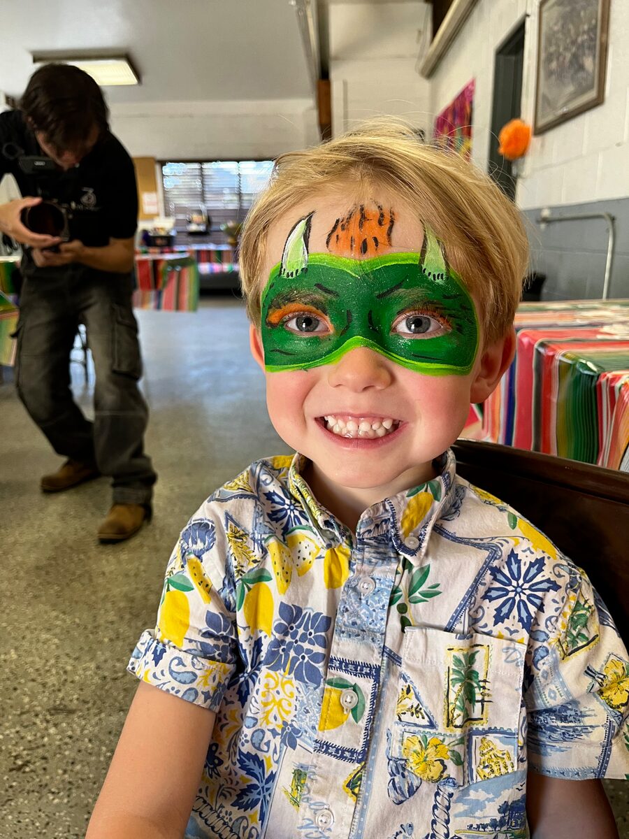 Young guest smiling in bright green superhero mask face paint